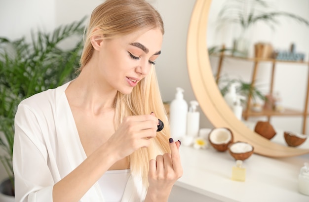 Junge Frau, die Kosmetik für Haare zu Hause verwendet