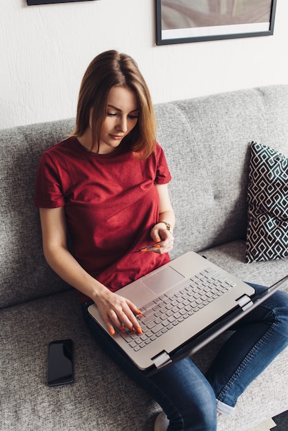 Junge Frau, die Kreditkarte hält, mit Laptop-Computer. Online-Shopping, von zu Hause aus bezahlen.