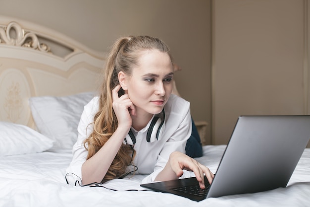 Junge Frau, die Laptop auf dem Bett benutzt