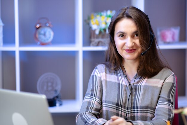 Junge Frau, die Laptop-Computer zu Hause verwendet und Headset trägt.