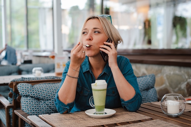 Junge Frau, die Matcha-Grüntee-Latte im Sommermorgen im Café genießt.