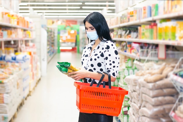 Junge Frau, die medizinische Einwegmaske beim Einkaufen im Supermarkt während des Ausbruchs der Coronavirus-Lungenentzündung trägt