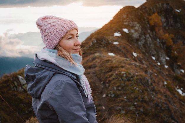 Junge Frau, die mit einem Rucksack in einem Hut lächelt und die Blicke auf die Berge bewundert