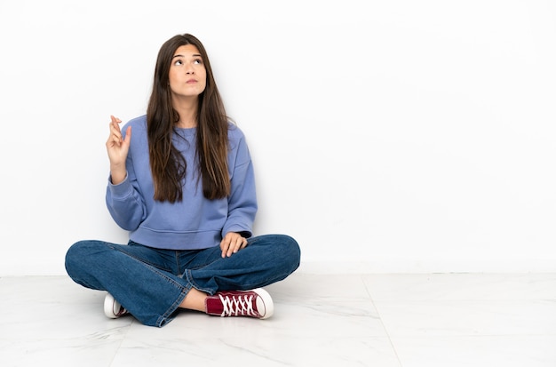 Junge Frau, die mit gekreuzten Fingern auf dem Boden sitzt und das Beste wünscht