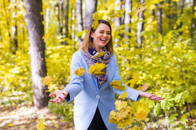 junge Frau, die mit Herbstlaub im Park spielt