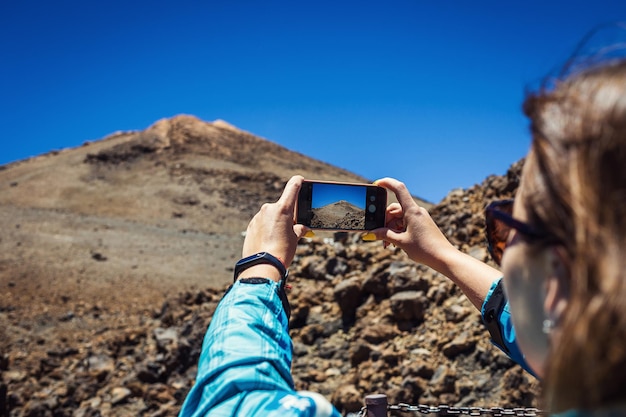 Junge Frau, die mit ihrem Handy ein Foto der atemberaubenden Berglandschaft auf Teneriffa Kanarische Inseln Spanien macht Reisekonzept