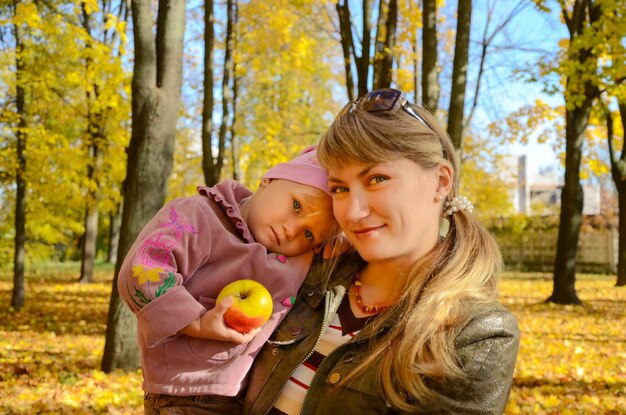 Junge Frau, die mit ihrem kleinen Kind im Park steht und einen Apfel hält