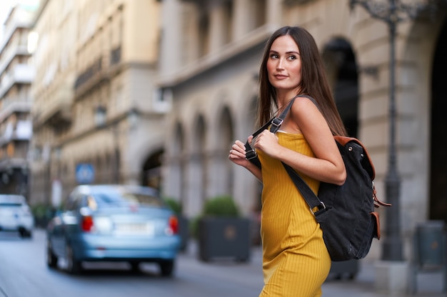 Junge Frau, die mit ihrem Rucksack auf dem Rücken eine Straße mit Verkehr überquert