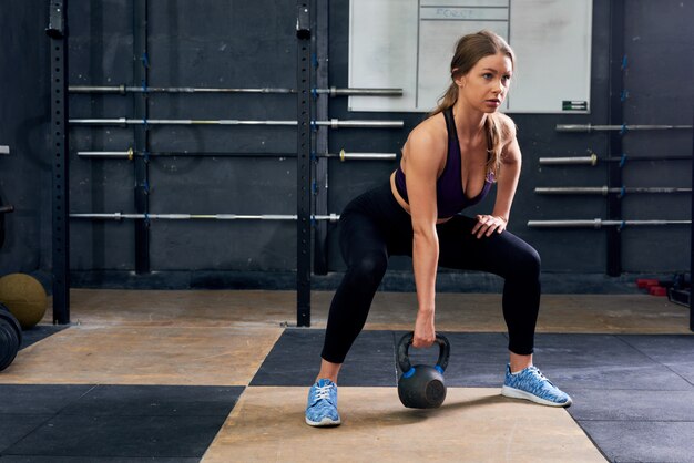 Junge Frau, die mit Kettlebells im Fitnessstudio hockt