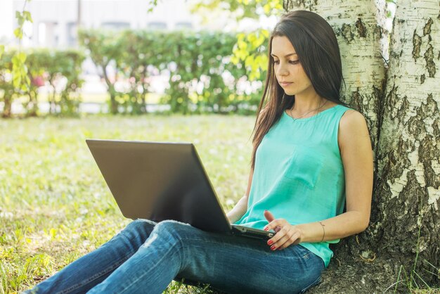 Junge Frau, die mit Laptop auf dem Rasen sitzt und tippt