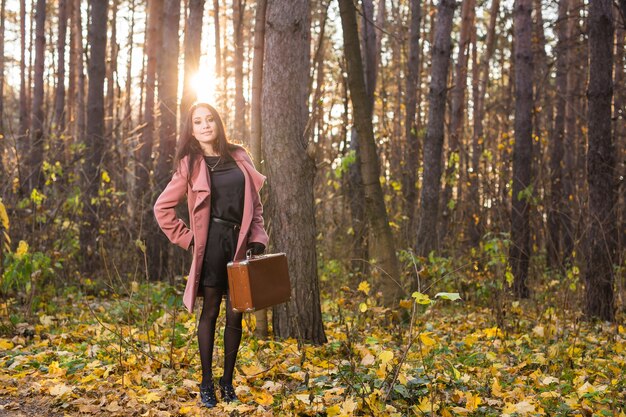 Junge Frau, die mit Retro-Koffer im Herbstpark steht