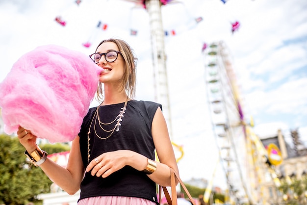 Junge Frau, die mit rosa Zuckerwatte vor dem Riesenrad im Vergnügungspark steht