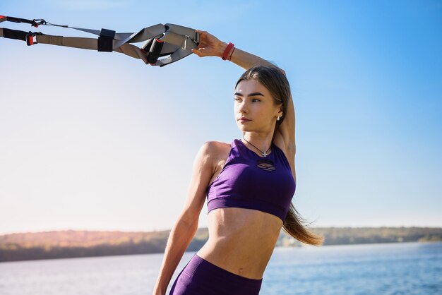 Junge Frau, die mit Suspension Trainer Schlinge im Park, nahe dem See trainiert.