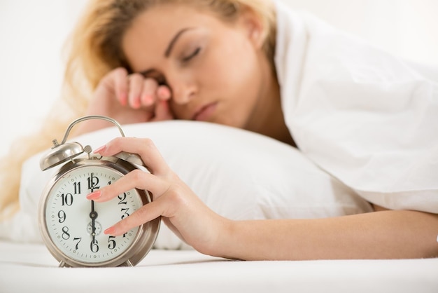 Foto junge frau, die morgens im bett liegt. sie wacht mit wecker auf.