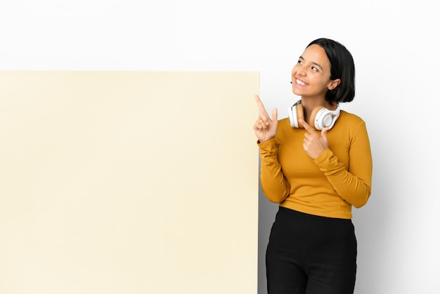 Junge Frau, die Musik mit einem großen leeren Plakat über isoliertem Hintergrund hört, der mit dem Zeigefinger eine große Idee zeigt