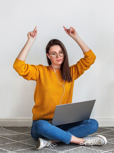 Junge Frau, die Musikkopfhörer und das Tanzen unter Verwendung des Laptops hört