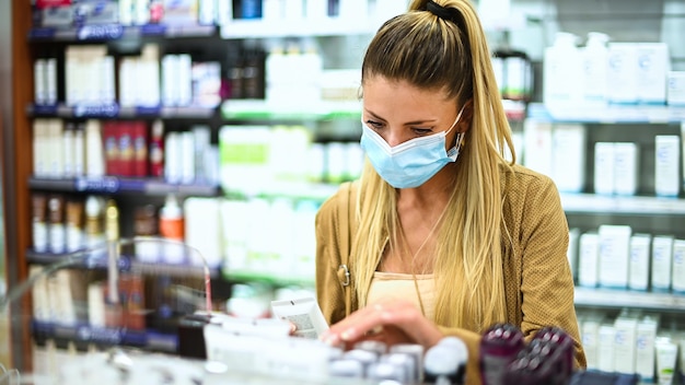 Junge Frau, die nach einem Produkt in einem Geschäft sucht, das eine Maske wegen Coronavirus trägt