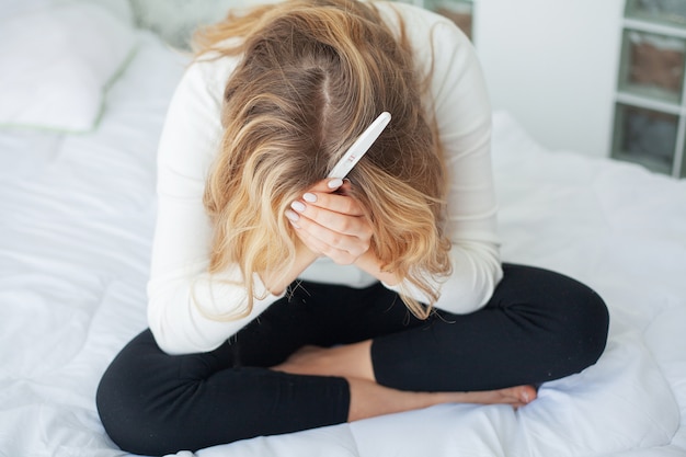 Junge Frau, die nach Schwangerschaftstestergebnis zu Hause betrachten deprimiert und traurig sich fühlt