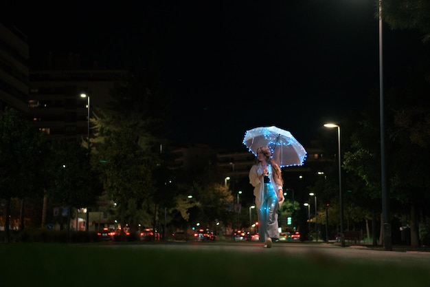 Junge Frau, die nachts mit Regenschirm mit Lichtern geht