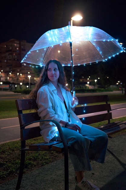 Junge Frau, die nachts mit Regenschirm mit Lichtern sitzt