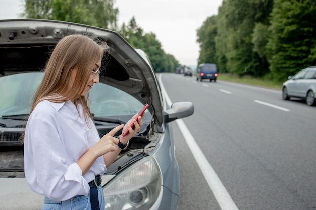 Junge Frau, die nahe kaputtes Auto steht