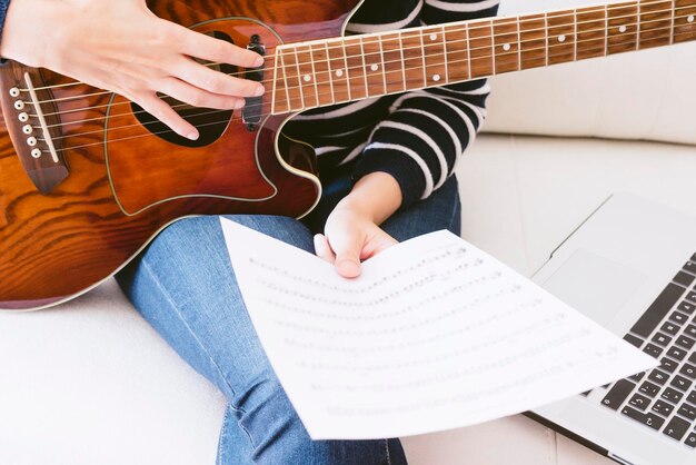 Junge Frau, die Noten mit Gitarre und Computer betrachtet Selektiver Fokus