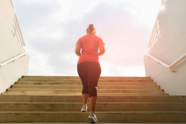 Junge Frau, die oben auf Steintreppe mit Sonnenfleckhintergrund läuft. Trainings- und Diätkonzept.