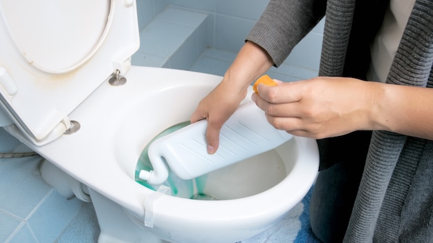 Junge Frau, die Reinigungschemikalie zum Reinigen der Toilette verwendet.