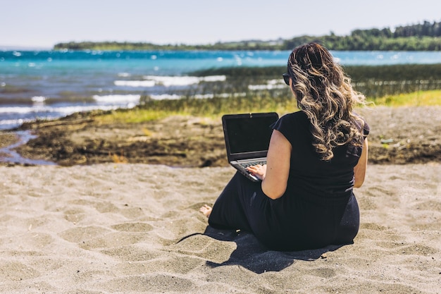 Junge Frau, die Remote-Online-Arbeit vom Strand aus macht Telearbeitskonzept Digitaler Nomade
