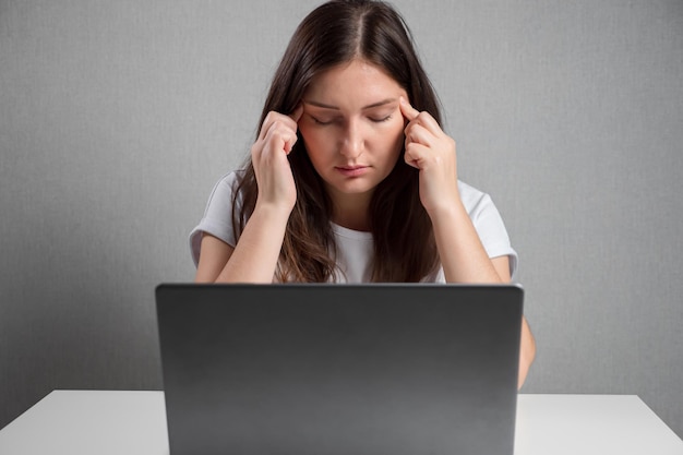 Junge Frau, die Schläfen massiert, während sie vor einem Laptop sitzt