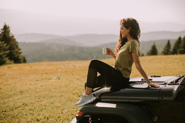 Junge Frau, die sich auf der Motorhaube eines Geländefahrzeugs auf dem Land entspannt