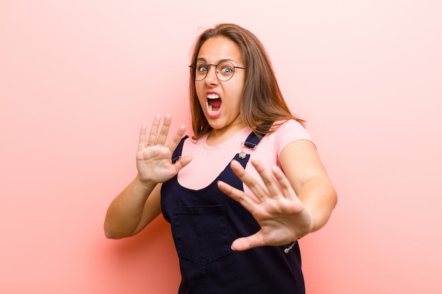 Junge Frau, die sich erschrocken fühlt, sich zurückzieht und vor Entsetzen und Panik schreit und auf einen Albtraum über der rosa Wand reagiert