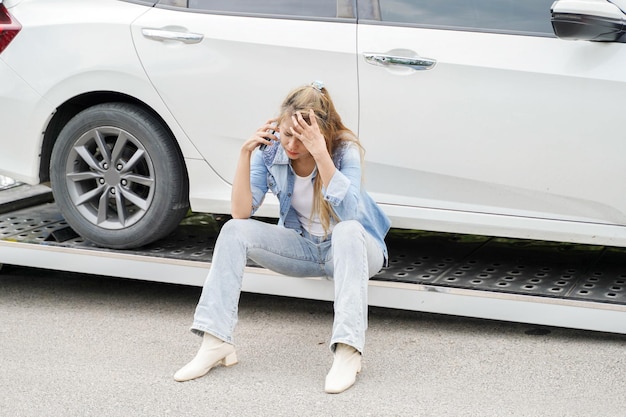 Junge Frau, die sich nach einem Autounfall im beschädigten Auto traurig fühlt, nutzt das Mobiltelefon, das die Versicherungsgesellschaft anruft