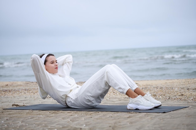 Junge Frau, die Situps auf der Yogamatte am Strand macht Foto in hoher Qualität