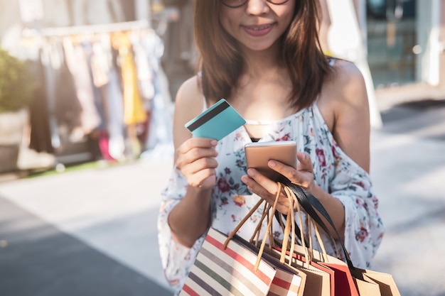Junge Frau, die Smartphone mit Einkaufstaschen und Kreditkarte am schwarzen Freitag verwendet