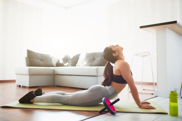 Junge Frau, die Sporttraining im Raum während der Quarantäne tut. Zurück auf Yogamatte strecken. Auf dem Bauch liegen und sich strecken.