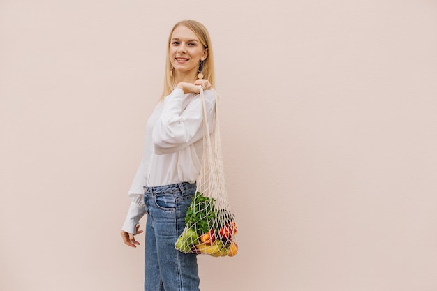 Junge frau, die string-einkaufstasche mit früchten hält. wiederverwendbare öko-tasche für einkäufe