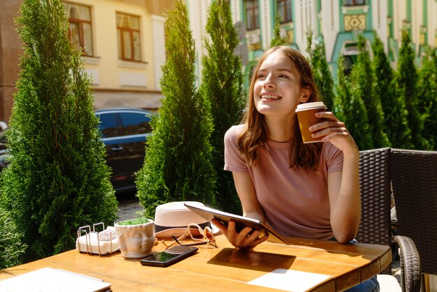 Junge Frau, die Tablet-PC in einem Café auf einer Sommerterrasse verwendet