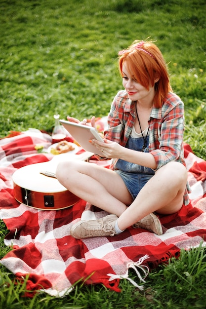 Junge Frau, die Tablette im Freien am Picknick und lächelnd verwendet