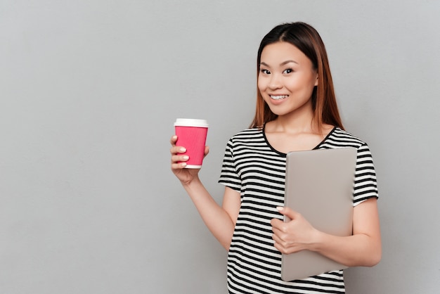 Junge Frau, die Tasse Kaffee und Laptop hält