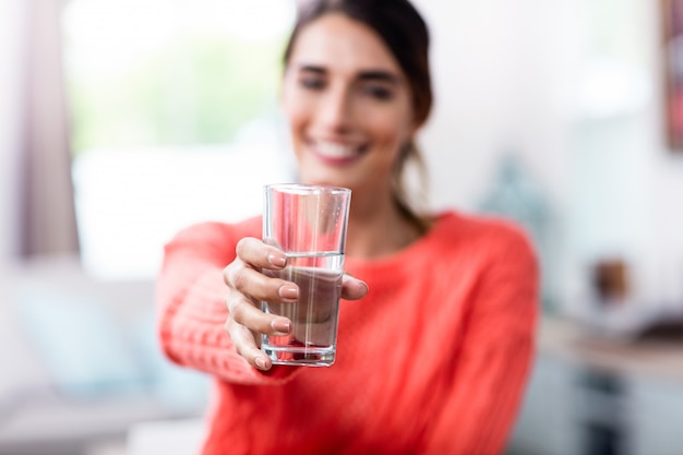 Junge Frau, die Trinkglas mit Wasser zeigt