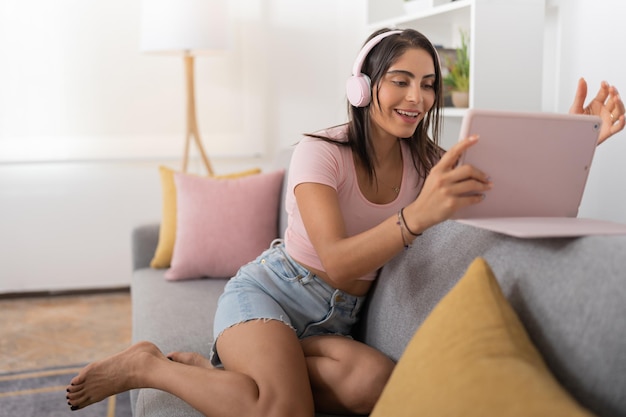 Junge Frau, die über ihre Kopfhörer einen Videoanruf mit ihren Freunden von ihrem digitalen Tablet aus tätigt