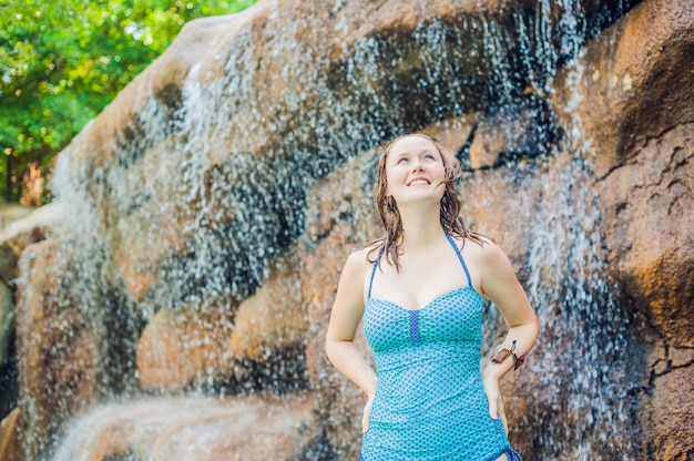 Junge Frau, die unter einem Wasserfall im Aquapark entspannt