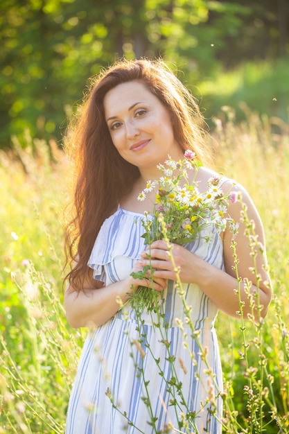 Junge Frau, die unter Wildblumen am sonnigen Sommertag geht