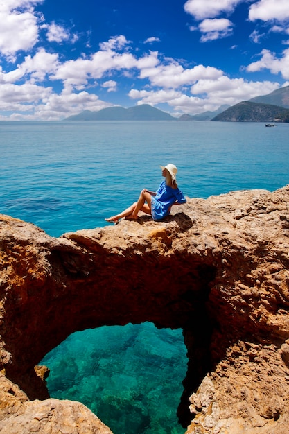 Junge Frau, die Urlaub auf Felsen mit luxuriösem Blick genießt, der Emotionen auf azurblauem Meereshintergrund zeigt. Glückliche Frau auf romantischer Reise viel Spaß im Sommerurlaub. Konzept Romantik und Entspannung