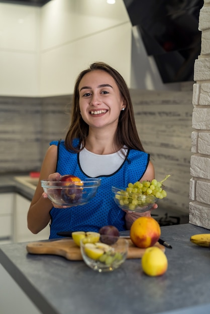 Junge Frau, die verschiedene Früchte schneidet, die gesundes Essen auf einem Kitche-Holztisch kochen. Geschirr zubereiten