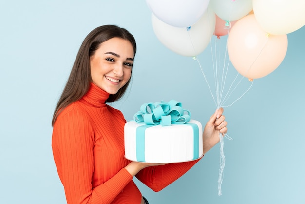 Junge Frau, die viele Luftballons lokalisiert auf blauer Wand fängt