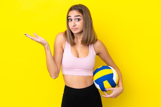 Junge Frau, die Volleyball auf gelbem Hintergrund spielt, die Zweifel hat, während sie die Hände hebt