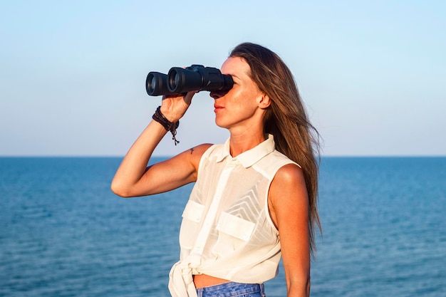 Junge Frau, die von der Klippe durch ein Fernglas auf das Meer schaut