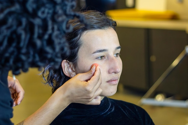 Foto junge frau, die von einem professionellen make-up-künstler in einem umkleidezimmer geschminkt wird